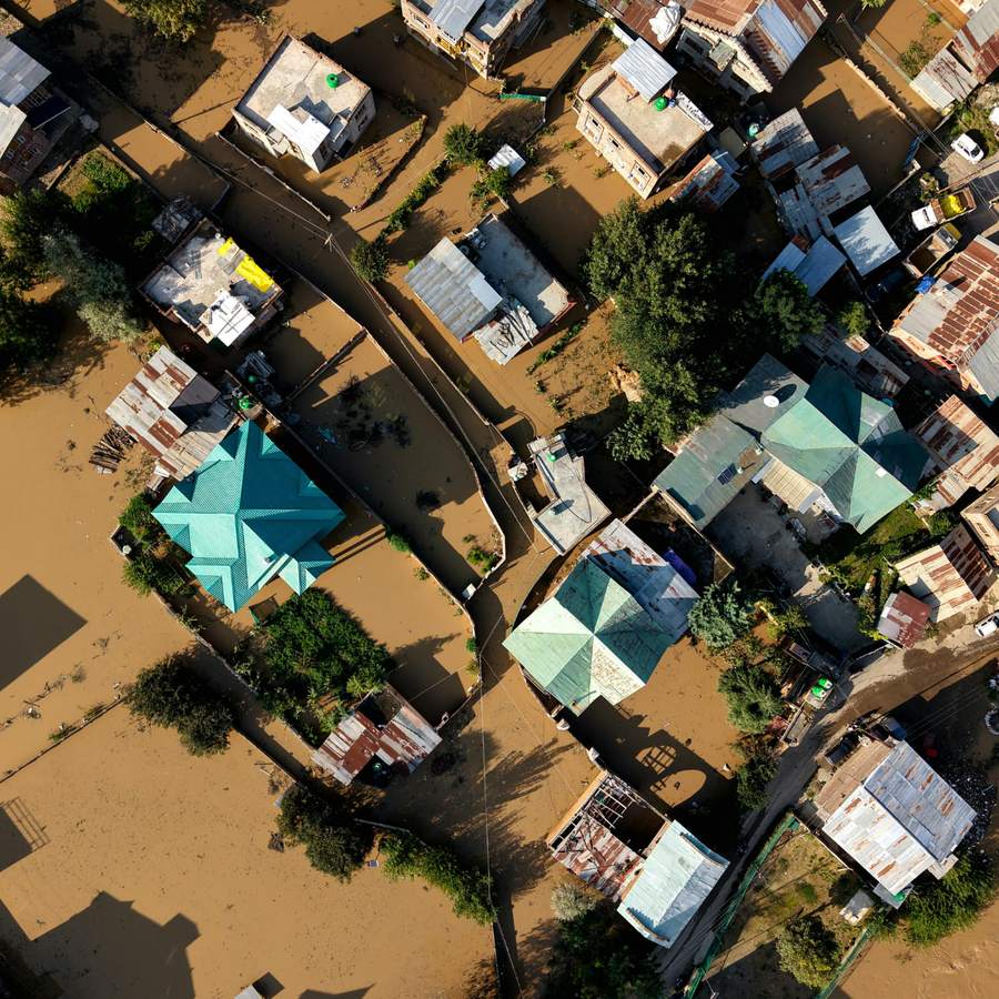 An overhead view of a settlement under brown floodwater, streets and yards submerged between the houses.